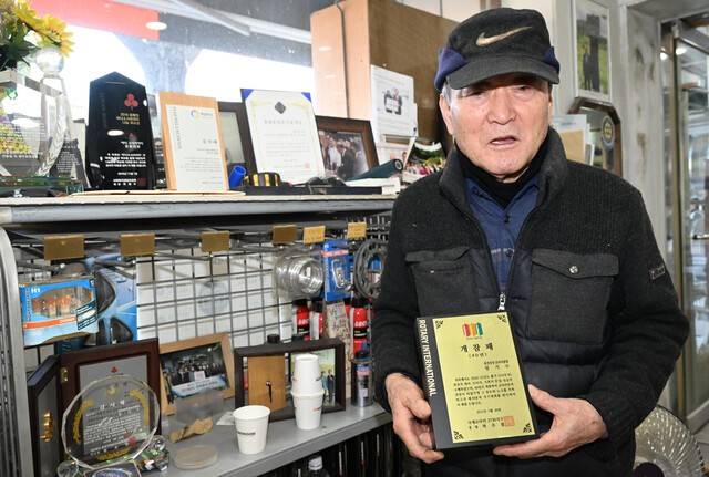 ▲ 3일 춘천 근화동 매장에서 임기수 한국타이어 춘천판매점 회장이 그동안 받았던 공로패를 배경으로 춘천중앙로타리클럽 개참패를 들어보이고 있다.