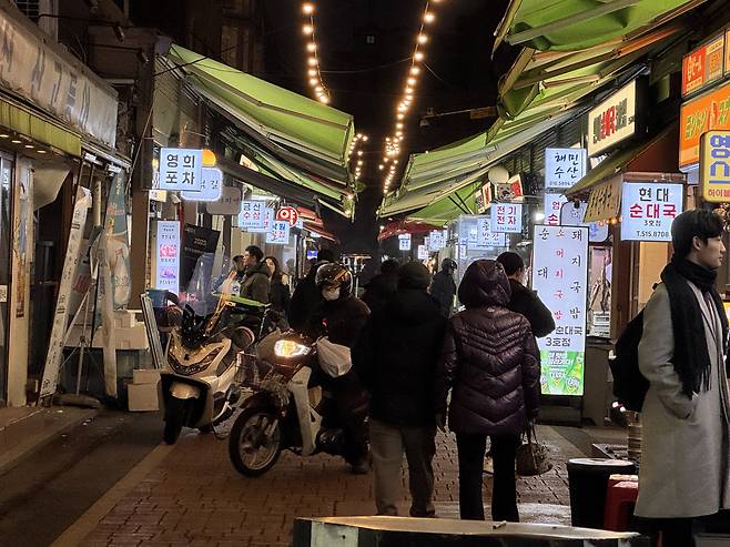 서울 강남구 영동전통시장 저녁 시간, 전구 조명이 켜진 상점들 사이로 사람들과 오토바이가 오가고 있다.(박상군 인턴 기자 kopsg@)