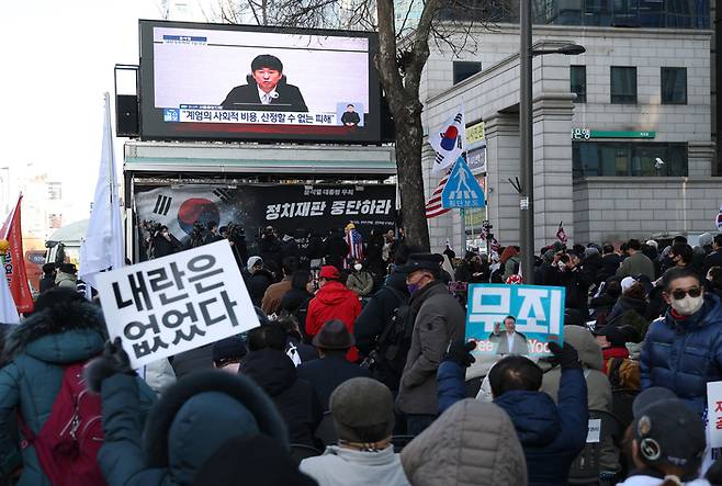 12·3 비상계엄과 관련해 내란 우두머리 혐의로 기소된 윤석열 전 대통령에 대한 1심 선고가 열린 지난 19일 서울 서초구 서울중앙지방법원 인근에서 지지자들이 관련 뉴스를 보고 있다. 이날 재판부는 윤 전 대통령에게 무기징역을 선고했다. [연합뉴스]