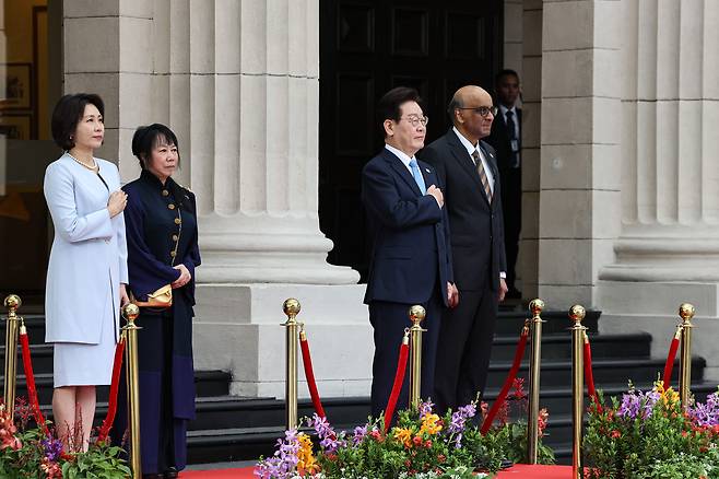이재명 대통령과 김혜경 여사가 2일 싱가포르 외교부 청사에서 열린 국빈방문 환영식에서 국기에 경례하고 있다. 이 대통령 오른쪽은 타르만 샨무가라트남 싱가포르 대통령.  [연합]