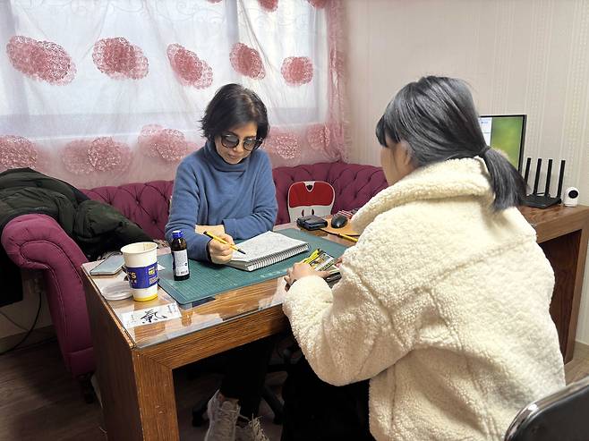 A fortune teller reads off a saju (fortune-telling based on birth charts) book for a customer at a shop in Gwangjin District, eastern Seoul, on Dec. 31, 2025. [JOONGANG ILBO]