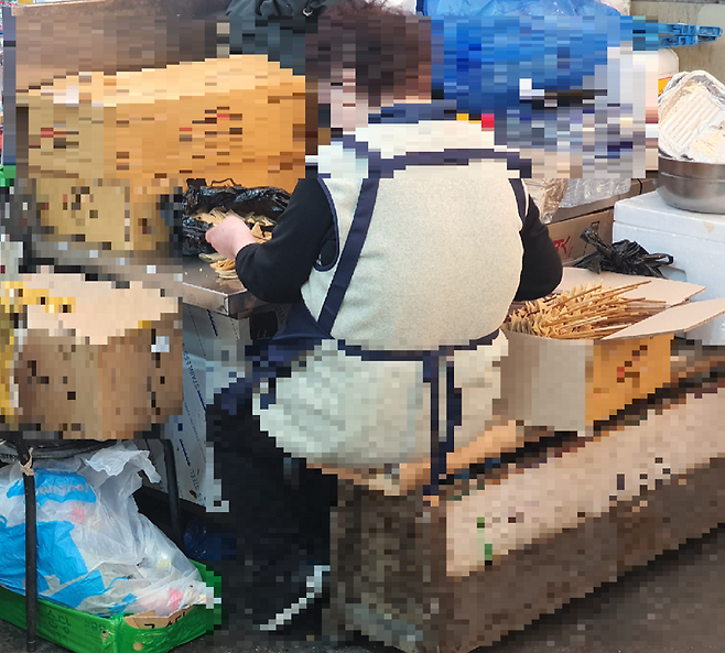 광장시장 한 노점 뒤편에서 상인이 음식 재료를 손질하고 있다. 그 옆에는 검게 변색된 나무 꼬치에 꿰인 어묵꼬치가 종이 상자에 담겨 있다. 사진=최승한 기자