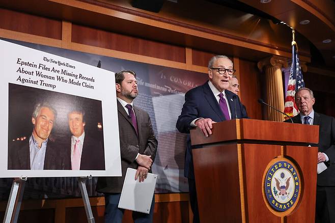 미국 의회에서 척 슈머 민주당 상원 원내대표가 지난달 26일 도널드 트럼프 대통령에게 엡스틴 파일의 전면 공개를 요구하는 기자회견을 하고 있다. 왼쪽 사진에는 과거 제프리 엡스틴과 트럼프의 친분을 보여주는 모습이 찍혔다. 로이터 연합뉴스