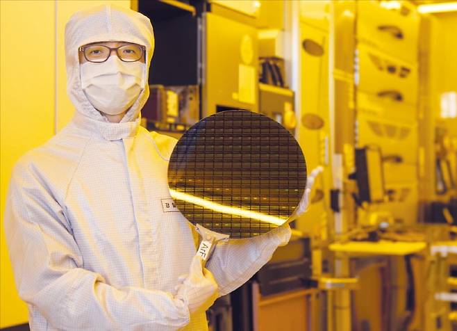 강일석 나노종합기술원 차세대플랫폼개발센터장이 12인치(300mm) 소자 반도체 웨이퍼를 들고 있다. 이 웨이퍼는 이 곳이 보유한 ASML사의 불화아르곤(ArF) 이머전 스캐너(뒤쪽 장비)를 사용해 제작했다. /나노종합기술원 제공
