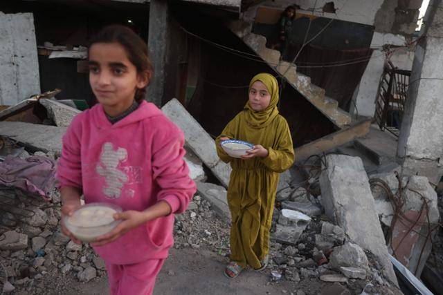 가자지구의 칸유니스 어린이들이 10일 부서진 건물 앞에서 음식을 들고 이동하고 있다. 칸유니스=AFP 연합뉴스