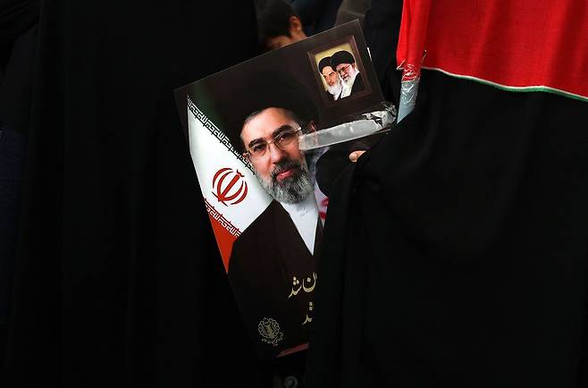 지난 9일(현지시간) 이란 수도 테헤란에서 차기 최고지도자로 선출된 모즈타바 하메네이를 지지하는 집회가 열렸다. 한 참가자가 모즈타바의 사진과 그의 아버지 알리 하메네이 그리고 이란의 영적 지도자 루홀라 호메이니의 초상화를 들고 있다. AFP=연합뉴스