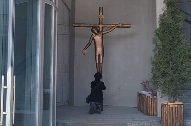 ▲ 이승훈베드로성지기념관 2층 상설 전시실로 올라가는 출입문 옆에 세워진 십자가상에 한 신자가 기도를 하고 있다. /인천일보DB