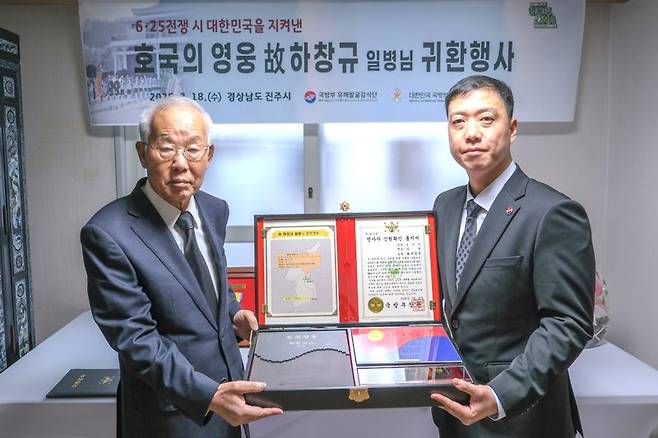 18일 오전, 경남 진주시 고 하창규 일병의 아들 하종복 씨(1951년생·74세, 왼쪽) 자택에서 열린 호국영웅 귀환행사에서 김성환 국방부 유해발굴감식단장 직무대리(육군 중령, 오른쪽)가 전사자 신원확인 통지서 등이 담긴 호국의 얼 함을 하종복 씨에게 전달하고 있다. 국방부 제공