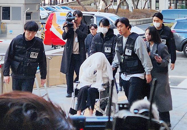 지난달 25일 약에 취한 상태로 외제 SUV 차량을 몰고 반포대교를 달리다 한강 둔치로 추락한 운전자 A씨가 27일 서울 마포구 서부지방법원에서 열린 구속 전 피의자 심문(영장실질심사)에 옷으로 얼굴을 가리고 휠체어를 탄 채 출석하고 있다. 연합뉴스