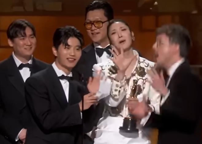 넷플릭스 애니메이션 영화 ‘케이팝 데몬 헌터스’의 주제곡 ‘골든’을 작곡한 더 블랙 레이블 소속 프로듀서 팀 아이디오(IDO)와 작곡가 24, ‘골든’을 작곡하고 직접 부른 이재(EJAE), 마크 소넨블릭이 15일(현지시간) 미 로스앤젤레스 돌비 극장에서 열린 제98회 아카데미 시상식에서 주제가상을 받은 뒤 무대 위에 올랐다. IDO의 일원인 이유한이 수상소감을 발표하는 도중 퇴장을 재촉하는 음악이 흘러나오자 이재가 당혹스런 표정으로 손짓을 하고 있다. 2026.3.15 로스앤젤레스 AP 뉴시스