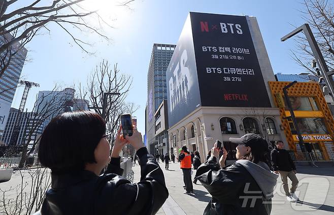 방탄소년단(BTS)의 서울 광화문광장 컴백 공연이 이틀 앞으로 다가온 19일 서울 종로구 광화문광장에서 시민들이 한 건물 외벽에 부착된 BTS 컴백 공연 광고물을 스마트폰으로 촬영하고 있다. 2026.3.19 ⓒ 뉴스1 김성진 기자