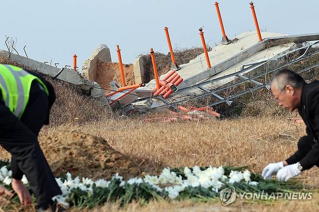 국화꽃 위 무너진 콘크리트 둔덕 (무안=연합뉴스) 김혜인 기자 = 12·29 제주항공 여객기 참사 1주기인 29일 무안국제공항 참사 현장에서 공항 관계자들이 국화꽃을 정리하고 있다. in@yna.co.kr