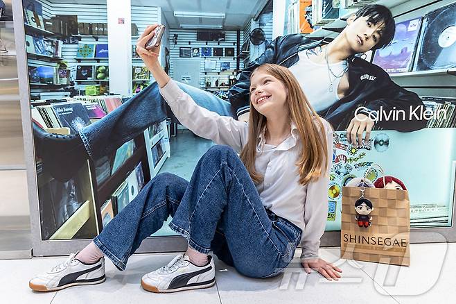 신세계면세점이 그룹 방탄소년단(BTS) 광화문 공연을 앞두고 K-컬처 콘텐츠와 쇼핑 혜택을 강화한다고 11일 밝혔다. 사진은 외국인 모델이 신세계면세점 명동점에서 BTS 콘텐츠를 배경으로 기념 촬영을 하는 모습. (신세계면세점 제공. 재판매 및 DB 금지) 2026.3.11 ⓒ 뉴스1