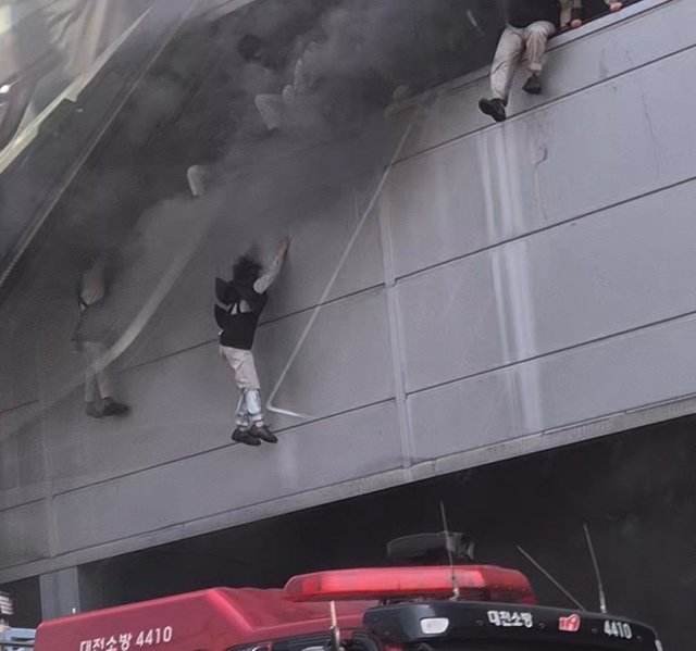 20일 오후 대전 대덕구 문평동 한 자동차부품 제조 공장에서 불이 나 검은 연기가 치솟는 가운데 직원들이 탈출을 위해 필사적으로 뛰어내리고 있다.  [독자 김영수 씨 제공=연합뉴스]