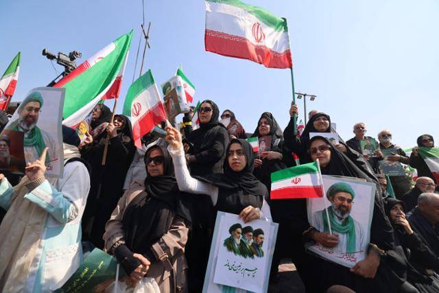 18일 이란 수도 테헤란에서 거행된 알리 라리자니 최고국가안보회의(SNSC) 사무총장과 이슬람혁명수비대 산하 바시즈 민병대의 골람레자 솔레이마니 총사령관의 장례식에 참석한 시민들이 이란 국기를 흔들고 있다. 두 사람은 이스라엘의 표적 공습으로 16일 사망했다. 테헤란=AFP 연합뉴스