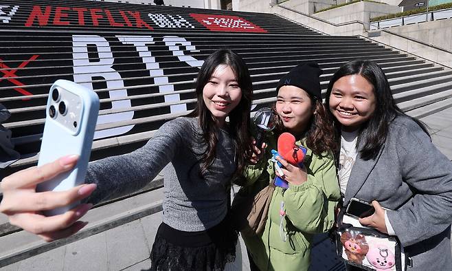 방탄소년단(BTS)의 서울 광화문광장 컴백 공연이 이틀 앞으로 다가온 지난 19일 서울 종로구 세종문화회관 계단에 마련된 BTS 컴백 공연 홍보물에서 외국인 관광객들이 기념촬영을 하고 있다. 뉴스1