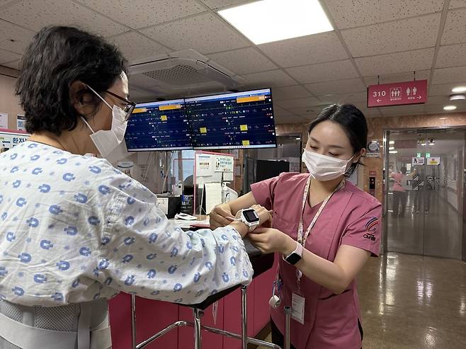 ある医療スタッフが患者にスマート病床モニタリングシステム「シンク」と連動するデバイス（白い腕時計型）を着用している（大雄製薬提供）