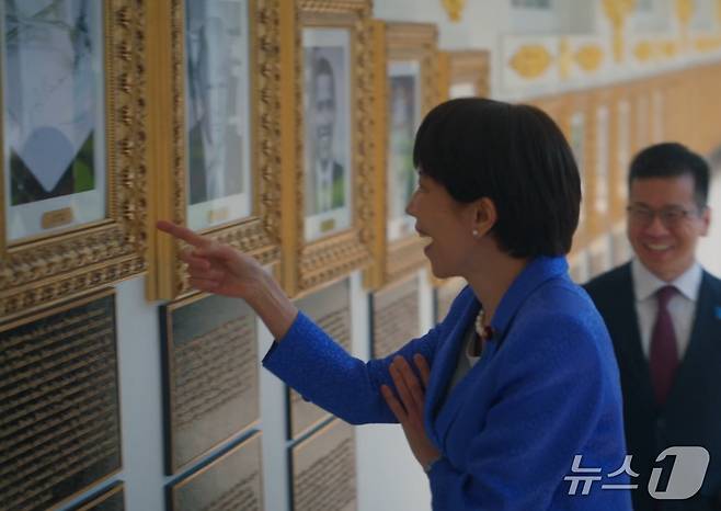 다카이치 사나에 일본 총리가 조 바이든 전 대통령의 초상화 자리에 그의 서명을 기계가 대신 그려주는 '오토펜' 사진이 걸려있는 것을 보고  웃음을 터뜨리고 있다. (백악관 X)