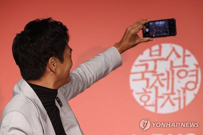 20203년 제28회 부산국제영화제에 참석한 홍콩 배우 저우룬파(주윤발)이 부산 해운대구 KNN시어터에서 열린 기자회견에서 개인 휴대전화로 기념촬영을 하고 있다. 저우룬파는 해당 셀카를 현장에 있는 아이폰 사용자에게 에어드롭으로 공유했다. [연합뉴스]