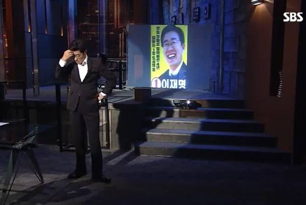 이재명 대통령의 조폭 연루설을 폭로한 2018년 7월 21일의 SBS '그것이 알고 싶다 권력과 조폭 - 파타야 살인사건 그 후 1년' 한 장면.&nbsp;진행자인 김상중 씨가 "이재명 변호사 이름이 등장해 당혹스럽다"며 한숨을 쉬며 손으로 머리를 짚고 있다.&nbsp;'그것이 알고 싶다' 다시 보기 화면 갈무리