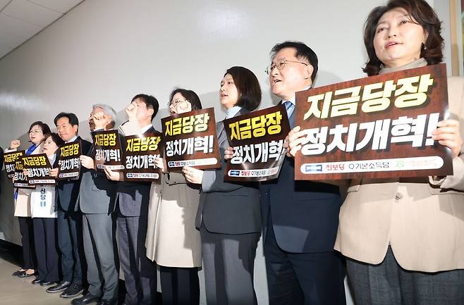 조국혁신당·진보당·기본소득당·사회민주당 등 진보 4당이 19일 국회 정치개혁특위 회의장 앞에서 정치개혁을 촉구하며 손팻말을 들고 구호를 외치고 있다. 연합뉴스