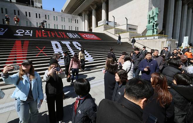 그룹 방탄소년단(BTS)의 컴백 라이브 아리랑(ARIRANG) 광화문 공연을 이틀 앞둔 19일 서울 종로구 세종문화회관에 설치된 홍보물 앞에서 아미(ARMY) 등 외국인 관광객들이 기념촬영을 하고 있다.(신태현 기자 holjjak@)