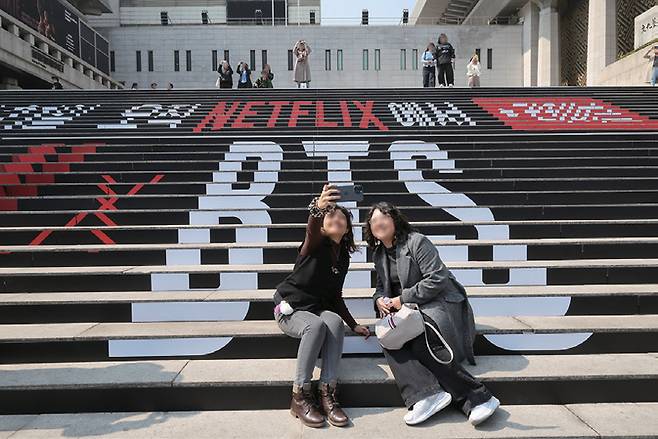 BTS의 서울 광화문광장 컴백 공연을 앞둔 3월17일 서울 종로구 세종문화회관 계단에서 외국인 관광객이 BTS 컴백 공연 관련 래핑 광고를 배경으로 기념촬영을 하고 있다. ⓒ시사저널 임준선