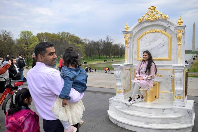 [워싱턴=AP/뉴시스] 30일(현지 시간) 미국 워싱턴DC 내셔널 몰에서 방문객들이 ‘왕에게 어울리는 왕좌‘(A throne fit for a king)라는 제목의 황금 변기에 앉아 기념 촬영을 하고 있다. 이 변기는 게릴라 예술그룹 ’시크릿 핸드셰이크‘라는 단체가 만든 것으로 백악관 리모델링에 집착하는 도널드 트럼프 대통령을 조롱하는 작품이다. 2026.03.31.