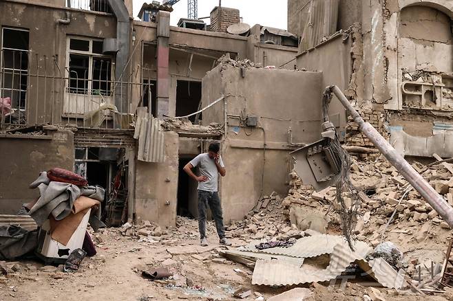 15일(현지시간) 이란 수도 테헤란에 대한 군사 공습 이후, 한 남성이 파손된 주택들 밖에서 휴대전화로 통화하고 있다. 2026.03.15. ⓒ AFP=뉴스1