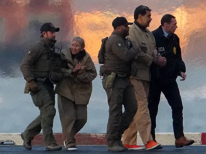 2026년 1월 5일 체포된 베네수엘라의 니콜라스 마두로 대통령과 그의 부인 실리아 플로레스가 DEA(마약단속국) 요원들의 호송을 받아 헬리콥터에서 내리고 있다. 니콜라스 마두로 대통령은 마약 테러, 공모, 마약 밀매, 자금 세탁 등 미국 연방 혐의로 뉴욕시의 다니엘 패트릭 맨해튼 연방 법원으로 이동해 첫 공판에 출석할 예정이다. /로이터 연합뉴스