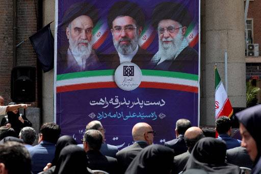 아야톨라 루홀라 호메이니(왼쪽부터), 알리 하메네이(오른쪽), 모즈타바 하메네이(가운데) 등 1979년 이후 이란의 최고지도자들 초상 앞에 앞에 이란 시민들이 앉아 있다.  (사진=AFP)