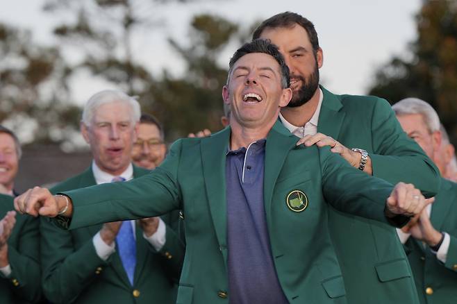 지난해 마스터스 정상에 올라 ‘커리어 그랜드슬램’을 달성했던 로리 매킬로이가 9일(한국시간) 개막하는 명인열전에서 2연패에 도전한다. 지난해 시상식에서 2024년 챔피언 스코티 셰플러의 도움을 받아 그린 재킷을 입으며 웃음을 짓고 있는 매킬로이(앞). 셰플러는 2년 만의 패권 탈환에 나선다. 오거스타 | AP뉴시스