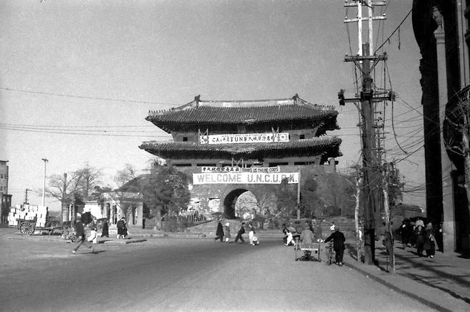 6. 25 전쟁 직후의 남대문, 차도와 인도의 구분도, 차도 빌딩도 보이지 않지만 남대문 모습은 그대로 있다. 플래카드에 'UN군 입성 환영'이라는 글씨가 눈에 띈다. 1950년대. / 사진가 김한용