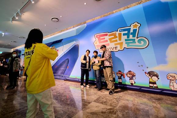 에피드게임즈의 심정선 부대표(좌측)와 한정현 대표가 '트릭컬 생존의 역사 전시회'를 찾은 팬과 기념사진을 촬영하고 있다. [사진=에피드게임즈]