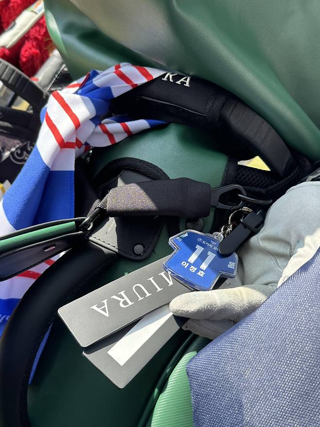 이정효 수원 삼성 감독이 13일 경기도 용인 코리아CC에서 열린 ‘2026 축구인 골프대회’ 도중 취재진에게 청백적 머플러와 키링을 보여주고 있다. 용인│사진공동취재단