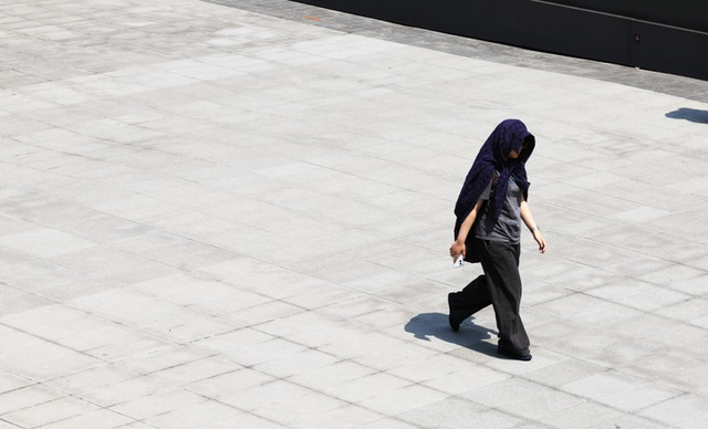 낮 최고기온이 27도까지 오르며 예년 기온을 웃돈 15일 서울 광화문 광장에서 한 시민이 겉옷으로 햇볕을 가리고 걷고 있다. [연합뉴스]