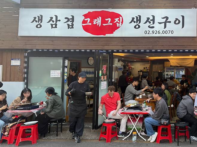 People grill sampyeopsal (pork belly) on grills at a plasttic table set-up outside a restaurant. [WOO JI-WON]