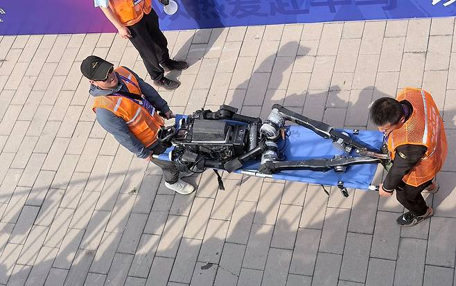 19일 중국 베이징에서 개최된 ‘베이징 이좡 휴머노이드 로봇 하프 마라톤’에 참가한 로봇이 결승선을 통과한 뒤 현장 요원에 의해 운송되고 있다. 신경진 특파원