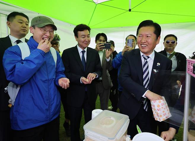 정청래(오른쪽) 더불어민주당 대표가 지난 18일 울산 남구 태화강 둔치에서 열린 ‘울산 자전거 대축전’을 찾아 자전거 페달을 굴려 팝콘을 튀기는 체험을 한 후 김상욱(왼쪽) 울산시장 후보, ‘영입인재 1호’ 전태진(가운데) 변호사와 팝콘을 나눠 먹고 있다. [연합]