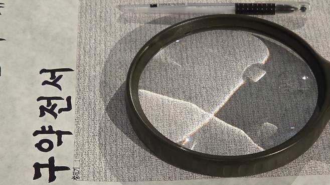 성경 필사전에 출품된 최일환 집사의 작품 위에 돋보기를 놓은 모습. 돋보기로도 잘 보이지 않을 정도의 작은 글씨로 썼다. /김한수 기자