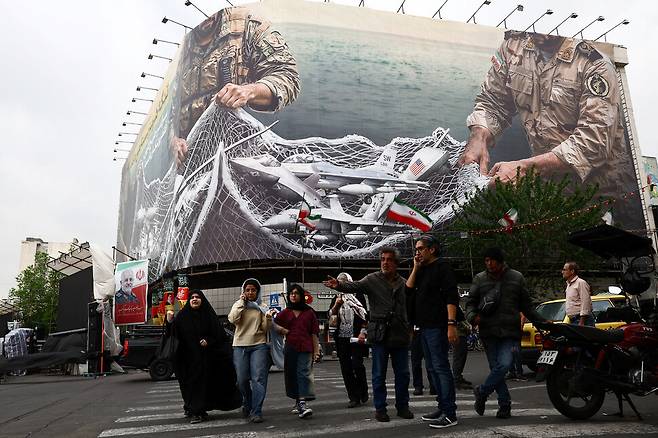 20일(현지시각) 이란 테헤란의 시민들이 미국의 최첨단 전투기들을 이란 군인들이 사냥하는 내용의 반미 선전물 앞으로 걷고 있다. WANA 로이터 연합뉴스