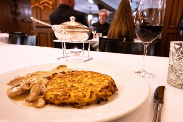 스위스 취리히 전통 음식 전문점 'zum kropf'의 게슈네첼테스. 음식 뒤로 따뜻한 온도를 유지하고 있는 소스 용기와 스위스산 피노 누아 와인이 보인다.