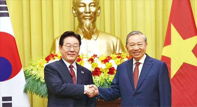 < ‘베트남 국부’ 호찌민 동상 앞에서 악수 > 이재명 대통령과 또럼 베트남 공산당 서기장 겸 국가주석이 22일 베트남 하노이 주석궁에서 정상회담에 앞서 악수하고 있다. 이 대통령과 또럼 서기장은 정상회담에서 중동 사태로 부각된 에너지 안보와 공급망 문제를 논의했다.  뉴스1