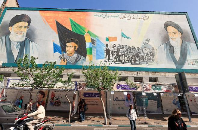 지난 16일(현지시간) 이란 테헤란에서 시민들이 이슬람혁명 지도자 고(故) 아야톨라 루홀라 호메이니와 이란 최고지도자 고 아야톨라 알리 하메네이의 모습이 그려진 벽화 옆을 지나가고 있다. (사진=로이터)