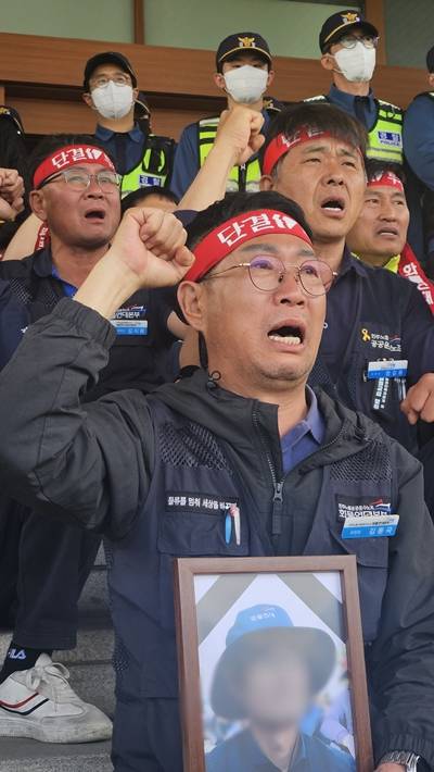▲김동국 화물연대본부 본부장이 2026년 4월21일 경남경찰청 앞에서 열린 '살인기업 CU BGF 규탄! 살인진압 경찰 공권력 규탄! 화물연대 긴급 기자회견'에서 서아무개 조합원의 영정사진을 들고 울먹이며 구호를 외치고 있다.