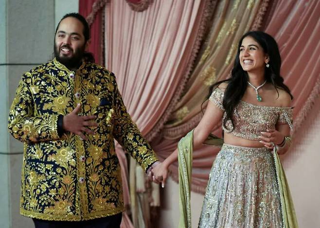 2024년 7월10일 인도 전통 결혼축하 행사인 ‘산기트’에 아난트 암바니(왼쪽)가 아내 라드히카 머천트와 손잡고 나타나고 있다. 로이터 연합뉴스