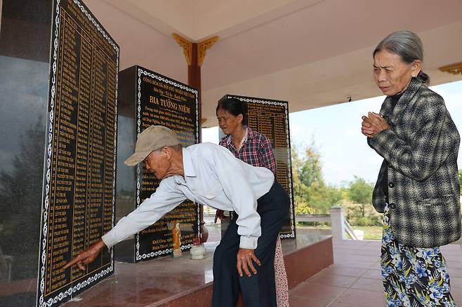 레륵(왼쪽)이 2026년 3월23일 베트남 다낭시 주이응이어사 선비엔촌의 주이응이어 학살 희생자를 추모하는 위령비에서 어머니 응오티드엉의 이름을 찾는 동안 그의 아내 쩐티리(오른쪽)가 두 손을 모은 채 이를 바라보고 있다. 가운데는 레륵 동생 레쯕의 아내 윈티탄.