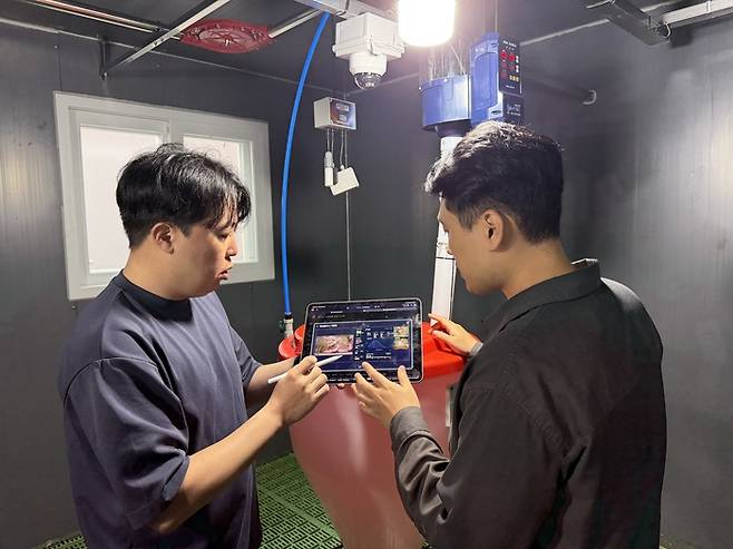 ETRI 연구진이 ‘제주형 양돈 AX 스마트팜’ 현장에서 스마트 기기를 이용해 돈사 내부 환경 제어 시스템을 점검하고 있다.[ETRI]
