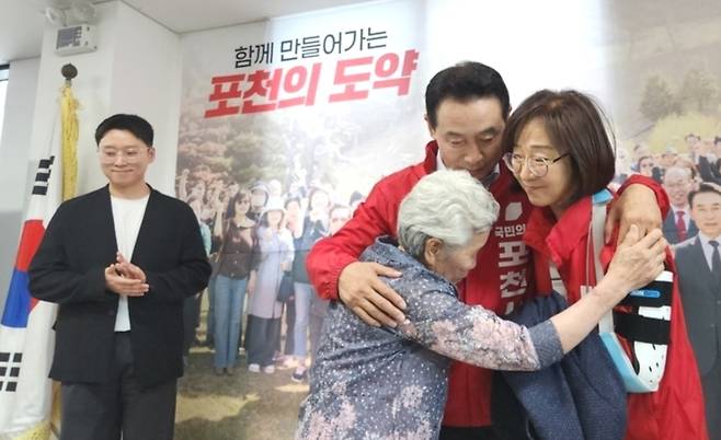 ▲ 국민의힘 백영현 포천시장 후보가 1일 선거사무소 개소식에서 고령의 어머니로부터 선거 운동복을 전달받은 뒤 감사의 인사를 전하고 있다. 백 후보는 이날 가족 전원이 조력자로 나선 '가족 원팀' 행보를 보였다. 이광덕 기자 kdlee@incheonilbo.com