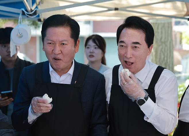 더불어민주당 정청래 대표와 박수현 충남도지사 후보가 1일 어버이날 기념 경로행사가 열린 충남 서산시문화회관 주차장에서 음식을 준비하며 떡을 먹고 있다. 연합뉴스